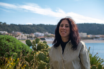 Dark-haired woman portrayed against the backdrop of the Tono bay, in Milazzo, Sicily. The woman is thirty-nine years old and wears a striped shirt