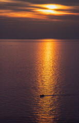 Sunset over the sea with strong orange reflections, and a boat crossing that reflection. From a viewpoint in Corniglia, Cinque Terre, Italy