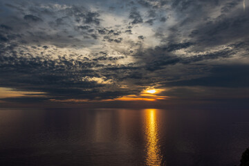 Sunset over the sea with a strong reflection of the sun on the water and clouds in the sky, from a viewpoint in Corniglia, Cinque Terre, Italy