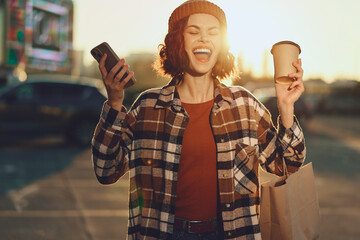 Woman with coffee and phone after shopping, smiling and laughing in urban sunlight, candid lifestyle portrait with authenticity, golden hour glow, mindful living and emotional storytelling.