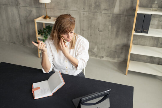 Businesswoman talking on phone and taking notes during home office work