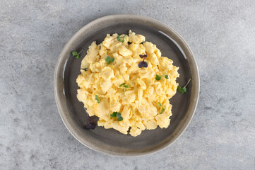 Scrambled eggs with green onions on a gray plate on a gray background. Healthy breakfast. Top view. 