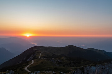 Spectacular sunrise from the Dobratsch summit in Carinthia, Austria. A winding hiking trail leads the eye across the alpine landscape towards the radiant sun rising over distant mountains and a valley