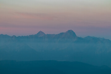 The iconic peaks of the Julian Alps stand tall above a sea of morning fog. A majestic and awe-inspiring alpine vista from the Dobratsch in Austria, colored by the soft pastel light of early dawn.