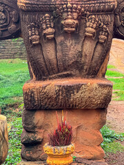 Detailed, weathered stone carving of a five-headed Naga serpent at Spean Praptos bridge in Cambodia, with burning red incense sticks placed at its base as a spiritual offering to the mythical guardian
