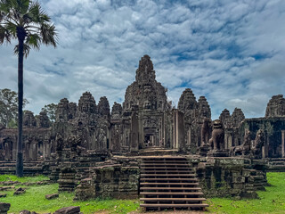 Majestic and sprawling Bayon temple, with its iconic face towers and guardian lion statues, stands under dramatic cloudy sky in the center of Angkor Thom, a world heritage site in Siem Reap, Cambodia.