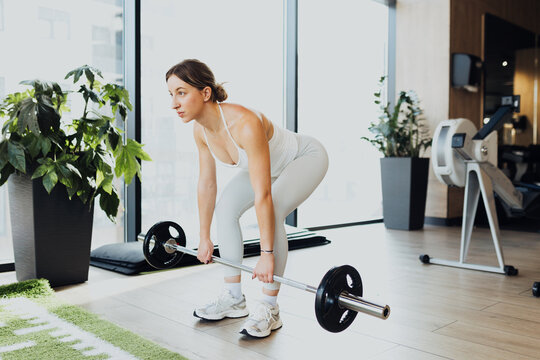 A young woman performing a deadlift in a modern gym. She is focused and motivated, lifting a barbell with proper form in a well-equipped fitness environment
