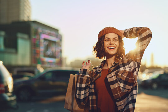 Woman shopping with paper bag, smile wide in city street at sunset, candid lifestyle and authenticity with golden hour glow, mindful living and emotional storytelling in urban fashion moment.