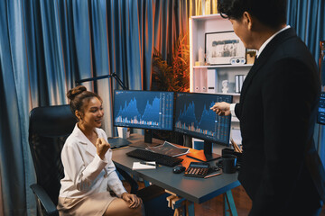 Successful business traders raising fist up with highest profit looking stock market online in real time at neon light modern office, pointing to dynamic financial graph on computer screen. Infobahn.