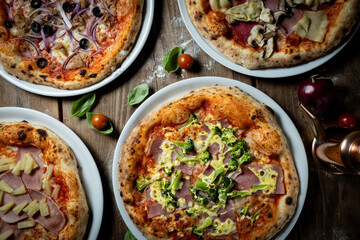 Pizzas aus dem Steinofen mit Gemüse, Brokkoli, Salami, Tomate, von oben fotografiert, mit Tomaten, Basilikum und Mehl auf dem Holztisch