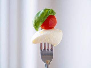 Fresh caprese bite with mozzarella, cherry tomato, and basil on a fork