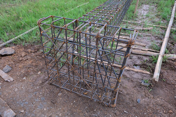 A close-up view of a reinforced concrete footing structure, commonly known as a “cakar ayam” foundation, made of steel rebar arranged in a grid pattern at a residential construction site