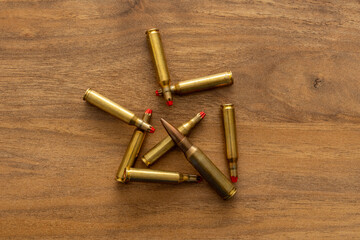 Overhead view of brass cartridges arranged in a radial cluster on a wood surface; the composition emphasizes metallic tones, pattern and an editorial concept linking ordnance with symbolic form.