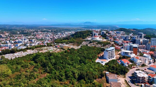 Rising above the green mountain with urban infrastructure. Vast cityscape on the shore of the Adriatic Sea in Montenegro. Aerial view.