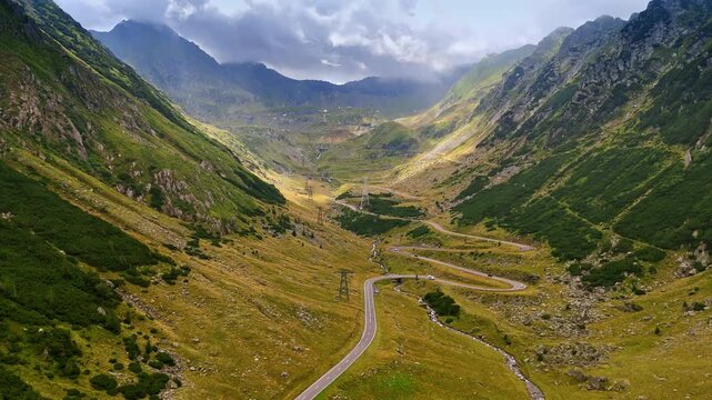 Beautiful valley with wavy road, narrow river and funicular line. Grey clouds in the sky among the mountains. Romania, the Carpathian Mountains.