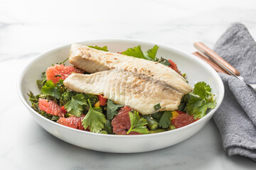 Fresh tilapia fillet with grapefruit salad on marble surface, top view.