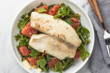 Fresh tilapia fillet with grapefruit salad on marble surface, top view.