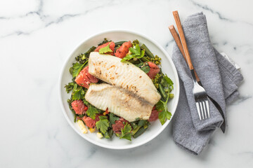 Fresh tilapia fillet with grapefruit salad on marble surface, top view.