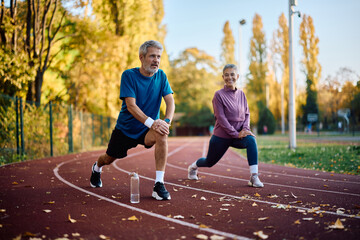 Mature sports couple warming up on running track at park. © Drazen
