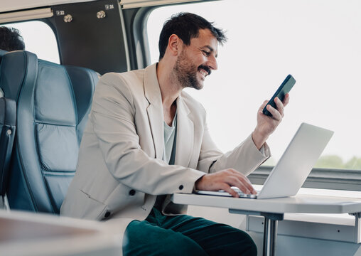 Man commuting on train using laptop and phone