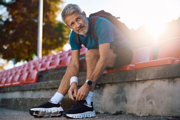 Mature sportsman tying shoelaces on his sneakers outdoors.