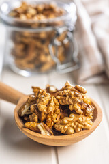 Peeled walnut kernels on wooden spoon on white table.