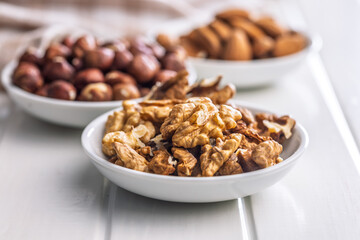 Peeled walnut, hazelnut and almond kernels in bowls on white table.