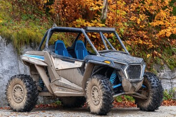 A muddy off-road vehicle sits parked near autumn foliage, showcasing its rugged design and all-terrain capabilities
