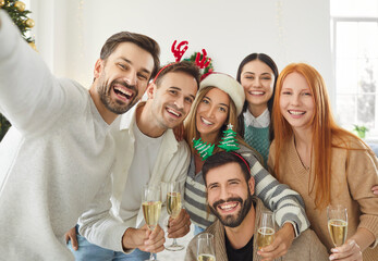 Friends gather for a group selfie on a phone during a Christmas or New Year party at home. The portrait captures holiday celebration and festive moments, ready to be shared on social media with joy.