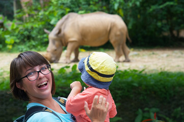 Happy woman with child watching a rhinoceros at the zoo