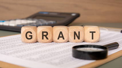 Wooden cubes spelling GRANT on financial papers, symbolizing non-repayable funding.