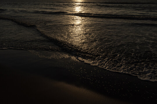 Olas oscuras rompiendo en la orilla con el reflejo dorado del sol poniente o naciente, capturado en la costa de C&oacute;rdoba, Colombia. Dramatismo, brillo y tranquilidad en el mar.