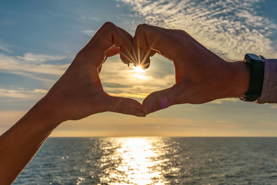 Hands heart sunset ocean view silhouette showing sunburst effect over sparkling water during golden hour - Powered by Adobe