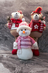Symbols of Christmas celebration. Soft toys of a snowman and decorated teddy bears on a brown marble background.
