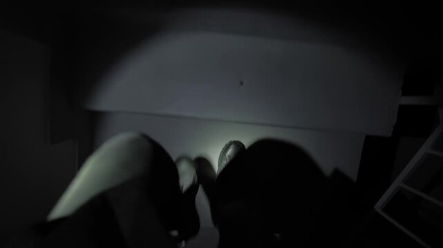 Man walks up a staircase in a high-rise building during a power outage. A flashlight provides the only visibility, illuminating the steps and surrounding concrete walls. A limited lighting conditions.