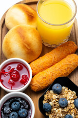 Delicious Latin American Breakfast Platter with Pandebono, Tequeños, Orange Juice, Granola, and Jams on a Wooden Tray on a White Background