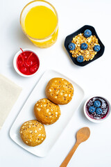 Healthy Continental Breakfast Flat Lay with Multigrain Buns, Granola with Blueberries, Orange Juice and Fruit Jams on White Background