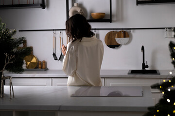 Woman in cream satin pajamas in the kitchen holds a cup of coffee in the morning Christmas. Preparation for winter holidays and New Year Eve. Happy young woman having fun and dreaming.