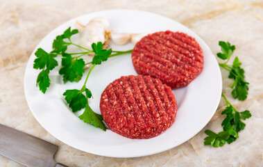 Raw beef patties for burgers with greens and garlic on table
