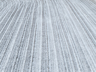 Aerial drone view of a plowed agricultural field covered in fresh white snow featuring rhythmic linear patterns and winter texture.