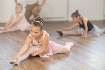 Children girls sit on floor and follow instructions of coach. Students do splits, prepare for training, perform muscle stretching.