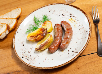 Two fried sausages with baked potatoes and herbs, served on the table for a hearty meal.