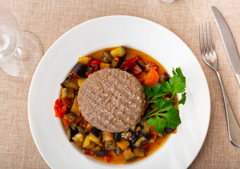 Beef cutlet with fragrant stewed vegetables on a white plate on the table. Hamburger patty with vegetables