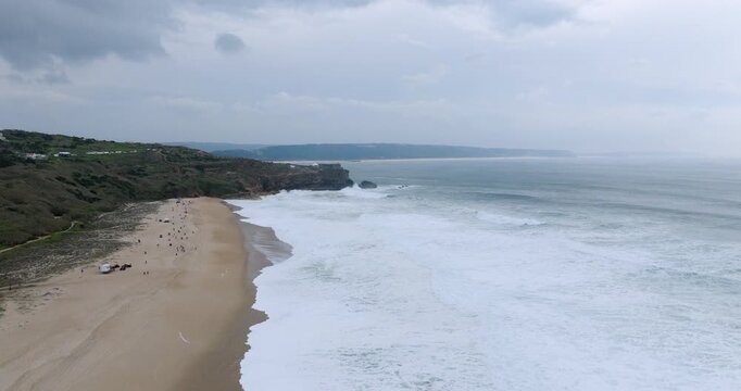 Ultra wide aerial panorama of Nazare extreme big wave surfing competition with cliff spectators, lighthouse and powerful Atlantic swell in Portugal