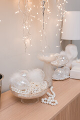 Stylish white Christmas decorations in the living room on the table: glass balls, pearls, feathers.