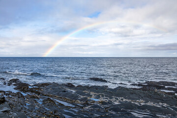 A captivating rainbow arcs over the St. Lawrence River in Quebec, creating a stunning natural spectacle against the rocky shoreline.