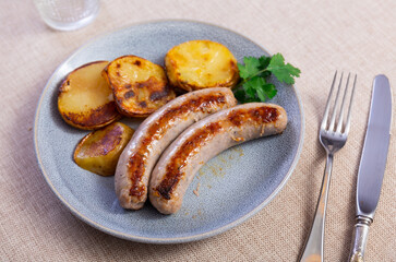 Two fried sausages with baked potatoes and herbs, served on the table for a hearty meal.