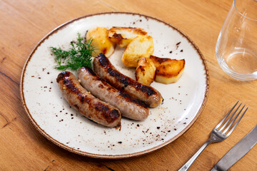 Grilled sausages with baked potatoes and herbs on a wooden table.