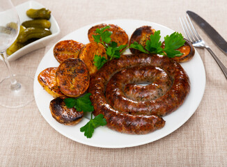 There are juicy fried sausages on plate, garnished with portion of baked potatoes. Dish is complemented with sprig of herbs, parsley, dill
