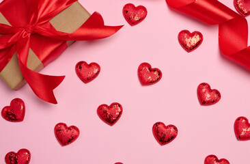 Gift box wrapped in craft paper and tied with a red satin bow on a pink background